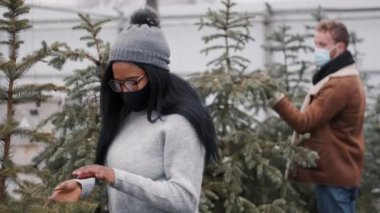 Çok ırklı maskeli çift markette Noel ağacı alışverişi yapıyor.