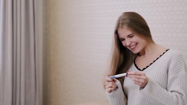 Ung dam känner sig glad över att bli gravid att hon lärt sig från graviditetstest hon håller medan hon sitter på sängen — Stockvideo