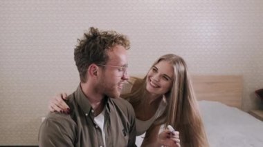 Mutlu çift yatakta hamilelik testine bakıyor.