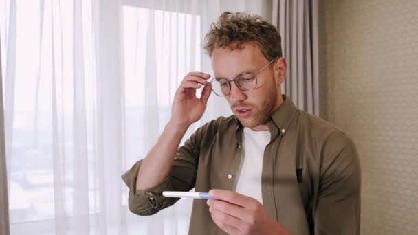 Разочарованный молодой человек смотрит на тест на беременность дома — стоковое видео