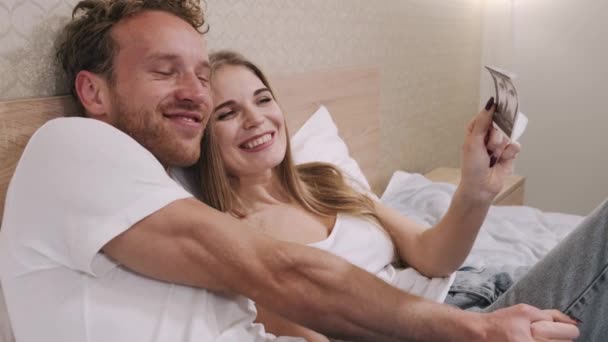 Pasangan hamil yang bahagia dan bersemangat melihat gambar USG bayi mereka di tempat tidur — Stok Video