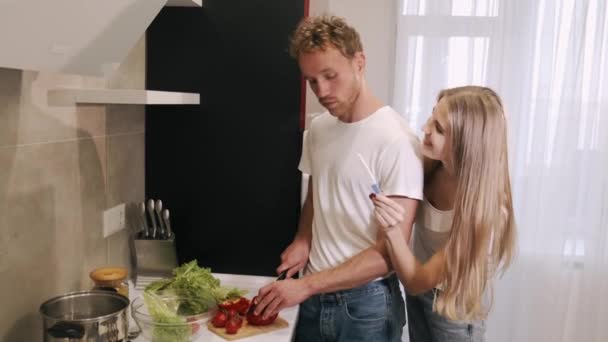 キッチンで良いニュースを共有しながら、夫に妊娠テストを示すコンテンツ魅力的な若い妻 — ストック動画