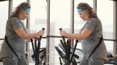 Orta yaşlı şişman kadın spor salonunda elips makinesi kullanıyor.