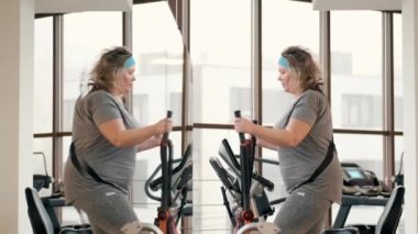 Orta yaşlı şişman kadın spor salonunda elips makinesi kullanıyor.