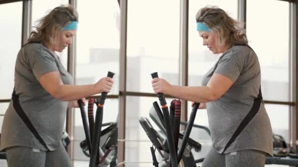 Middle aged overweight woman using ellipse machine at gym — Stock Video
