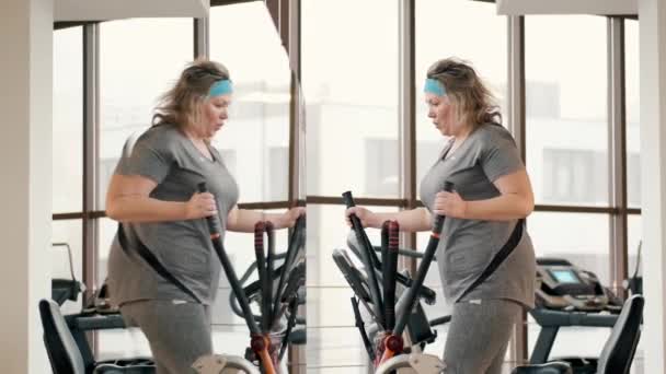 Kobieta w średnim wieku z nadwagą za pomocą elipsy na siłowni — Wideo stockowe