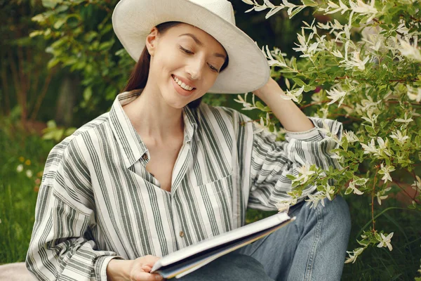 Kobieta w kapeluszu z książką w ogrodzie — Zdjęcie stockowe