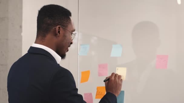 L'uomo d'affari afroamericano si trova vicino alla parete di vetro in ufficio per sviluppare la strategia o il piano aziendale — Video Stock