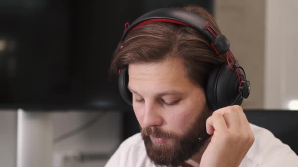 Jovem sério operador de call center do sexo masculino fazendo seu trabalho com um fone de ouvido — Vídeo de Stock