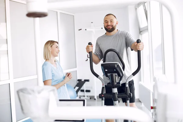 Ασθενής κάνει άσκηση με ποδήλατο σπιν στο γυμναστήριο με θεραπευτή — Φωτογραφία Αρχείου