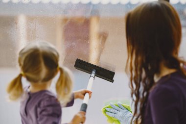 Kız ve anne pencereyi birlikte temizliyor.