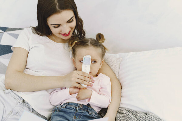 Мать с термометром сидит рядом с дочерью