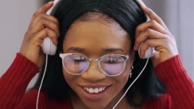 Kulaklıklı, dizüstü bilgisayarlı, evde çalışan Afrikalı genç bir kadın.