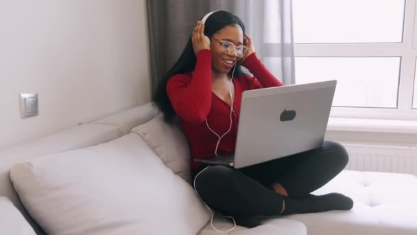 Junge Afrikanerin mit Kopfhörer und Laptop arbeitet zu Hause — Stockvideo