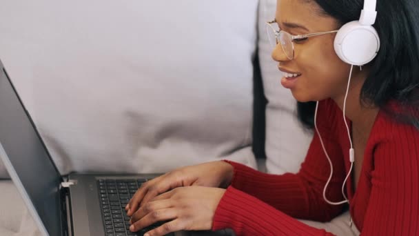 Jovem africana em fones de ouvido com laptop trabalhando em casa — Vídeo de Stock