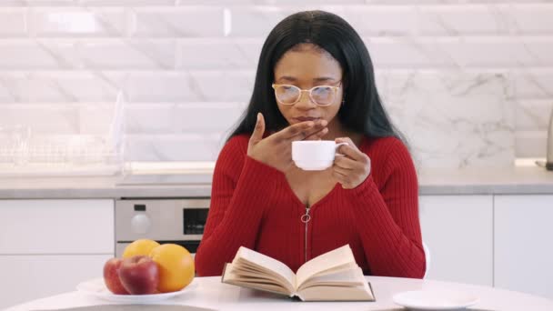 Menina afro-americana bebendo café e estudando em casa na cozinha — Vídeo de Stock