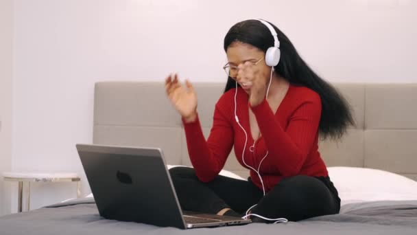 Ung afrikansk amerikansk kvinna njuter lyssna på musik på laptop när du ligger på sängen — Stockvideo