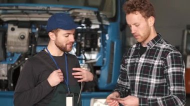 Genç otomotiv teknisyeni erkek müşteriyle konuşuyor.
