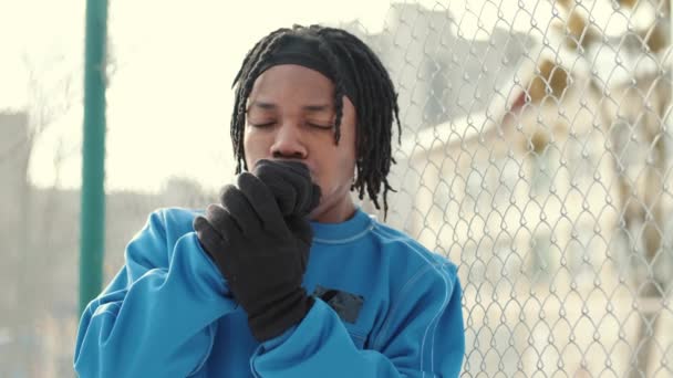 Afroamerykanin w rękawiczkach stojący na zewnątrz w zimie i rozgrzewający ręce — Wideo stockowe