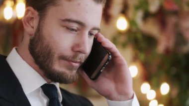 Ciddi derecede şık giyinmiş bir adam telefonla konuşuyor ve kafede çalışıyor.