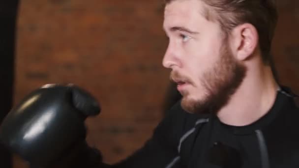 Jovem dedicado puncionando saco de boxe no ginásio — Vídeo de Stock