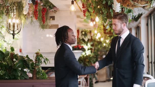 Dos hombres de negocios oficialmente vestidos se dan la mano en el hermoso restaurante — Vídeos de Stock