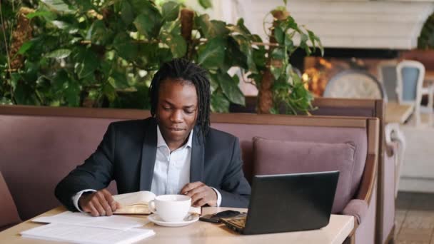 Hombre de negocios enfocado worjing en un café con ordenador portátil y papeles — Vídeo de stock