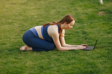 Çimlerin üzerinde oturan ve dizüstü bilgisayar kullanan bir kadın.