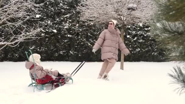 Joven madre feliz y su hija disfrutando de un paseo en trineo en un hermoso patio trasero cubierto de nieve — Vídeo de stock