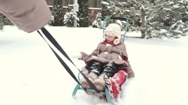 Junge glückliche Mutter und ihre Tochter genießen eine Schlittenfahrt in einem schönen verschneiten Hinterhof — Stockvideo