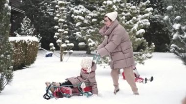 Genç mutlu anne ve kızı güzel bir bahçede kızakla geziyorlar.