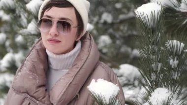 Kışın sıcacık giysiler içinde güzel bir kadın ve karla kaplı köknar ağaçlarının yanında gözlük..