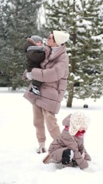 Sevimli anne ve bebek çocuklar güneşli dondurucu bir günde birlikte eğleniyorlar.