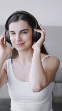Kulaklıklı genç bir kadın evde müzik dinliyor.