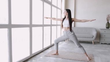 Atkuyruklu esmer, genç ve formda bir kız, parlak odada paspas üzerinde egzersiz yapıyor.