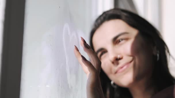 Young woman in hoodie near window on rainy day — Stock Video