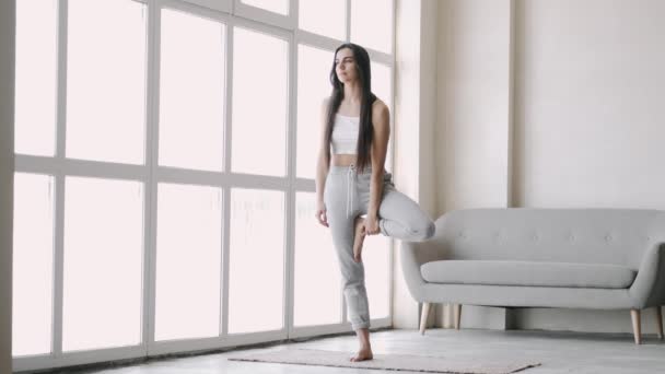 Ung passform sportig brunett flicka med pigtail, gör övningar på matta i ljust rum — Stockvideo