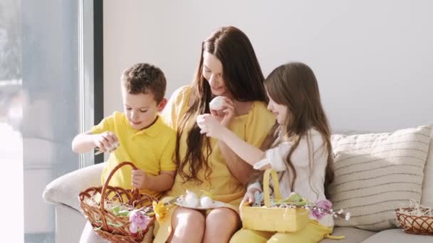 Досить молода мати в жовтій сукні, сидячи з дітьми на тренері на Великдень — стокове відео