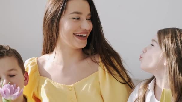 Mooie jonge moeder in gele jurk zitten met kinderen op coach op Pasen — Stockvideo