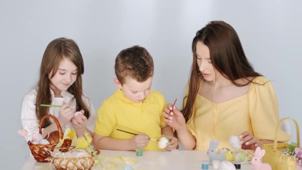 Madre colorear huevos de Pascua con sus hijos en la habitación blanca — Vídeo de stock