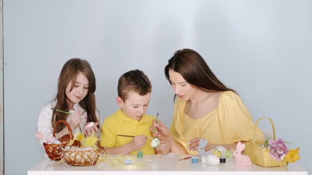 Madre colorear huevos de Pascua con sus hijos en la habitación blanca — Vídeo de stock