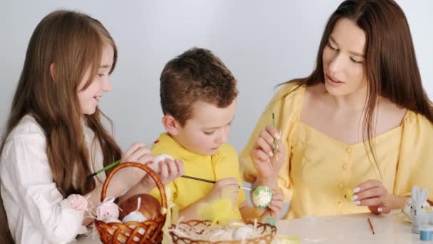 Мать раскрашивает пасхальные яйца с детьми в белой комнате — стоковое видео