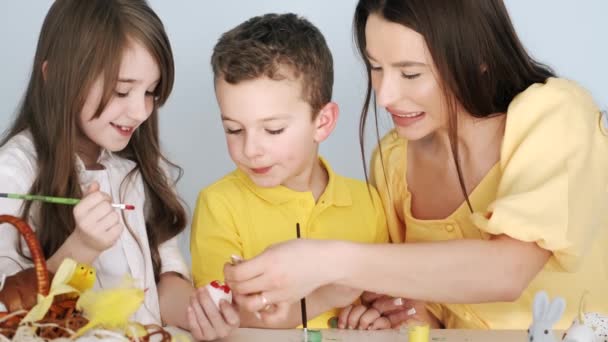 Mãe colorindo ovos de Páscoa com seus filhos na sala branca — Vídeo de Stock