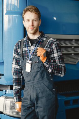  Tulumlu ve turuncu eldivenli bir adam mavi bir kamyonun yanında duruyor.