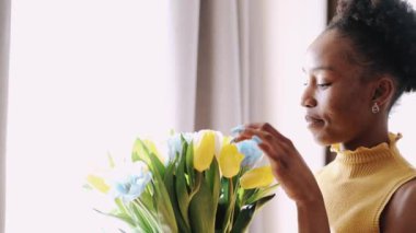 Afrikalı Amerikalı kadın gülümsüyor ve lalelere bakıyor.