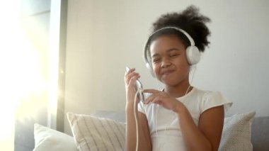 Güzel Afro-Amerikalı çocuk kulaklık takıyor ve cep telefonundan müzik dinliyor.