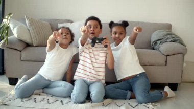 Mutlu Afro-Amerikan çocukları evde joystick ile video oyunu oynuyorlar.