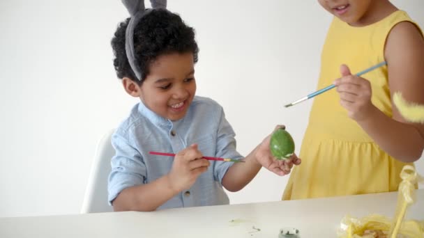 Африканские американские дети в смешных кроличьих ушах раскрашивают яйца на Пасху — стоковое видео