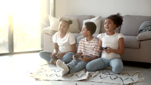 Щасливі афроамериканські діти грають у відеоігри з джойстиком вдома. — стокове відео