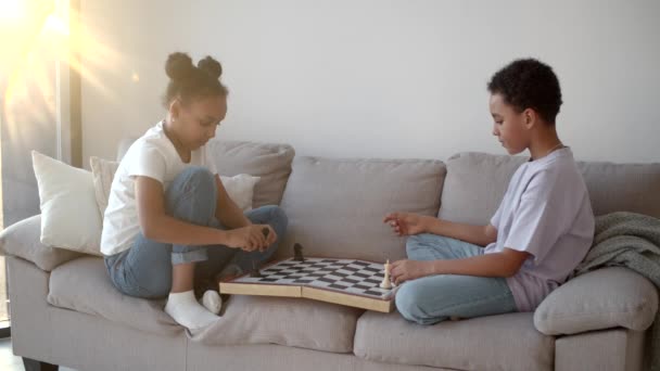 Hermano y hermana afroamericanos jugando al ajedrez en el sofá en la sala de estar — Vídeos de Stock